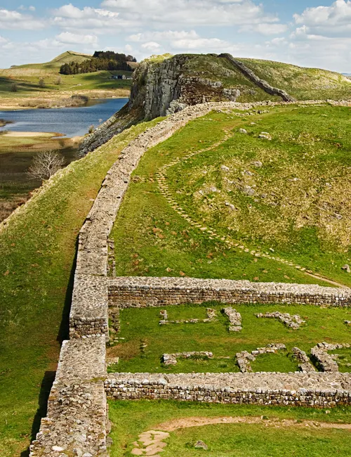 Hadrian's Wall winding across green hills beside a lake in northern England