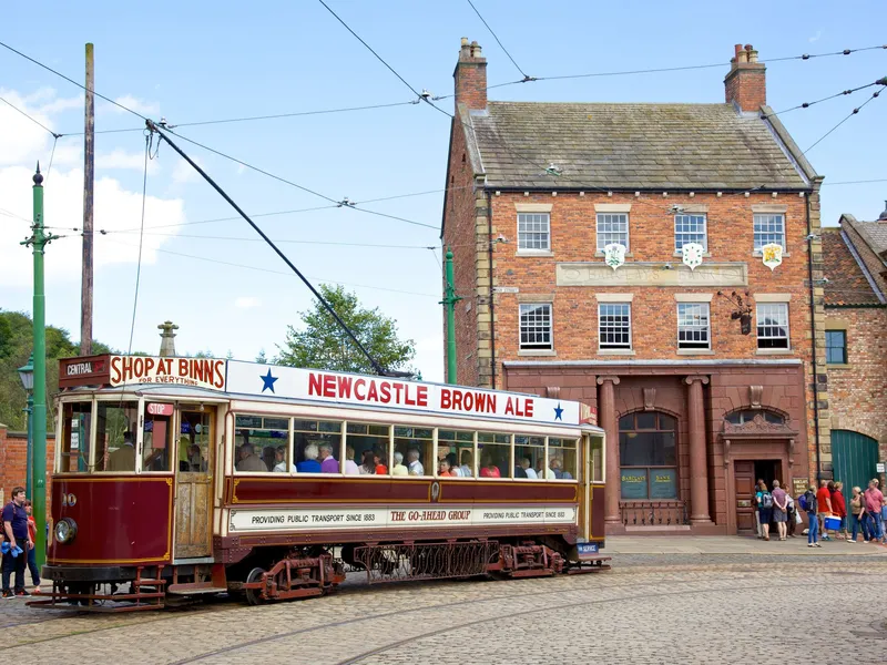 Historic Newcastle Brown Ale tram outside a brick Barclays Bank building, with passengers and pedestrians on a cobbled street.