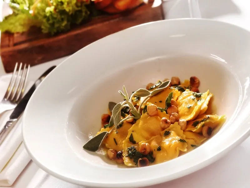 Bowl of golden ravioli topped with toasted hazelnuts and fresh sage