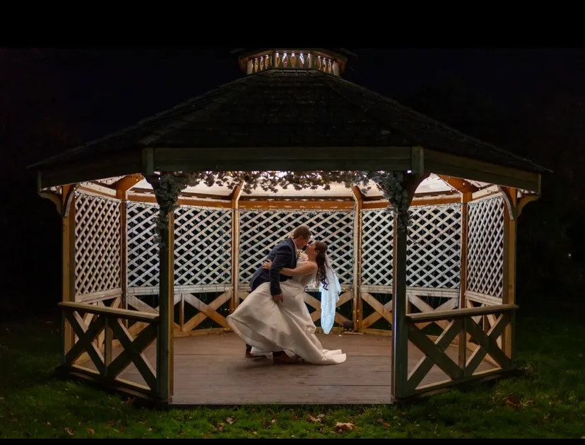 Newlywed couple kissing beneath a softly lit wooden gazebo at night