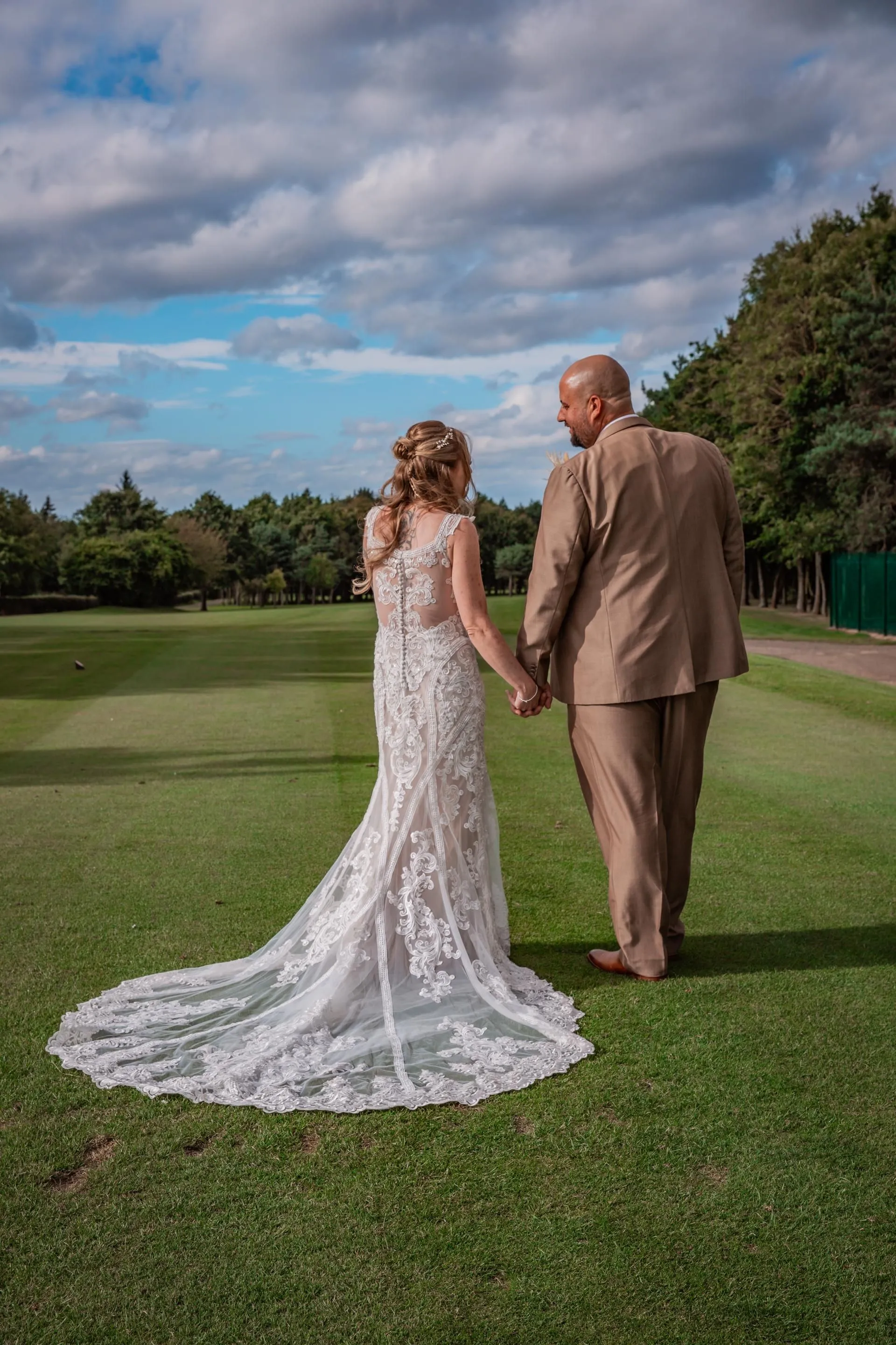 Bride and groom holding hands on a golf course beneath a dramatic cloudy sky