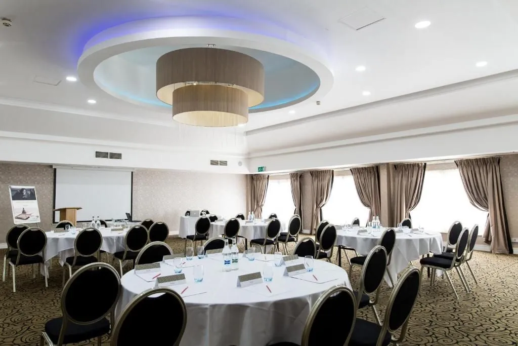 Elegant conference room with round tables, black chairs and a large circular chandelier.