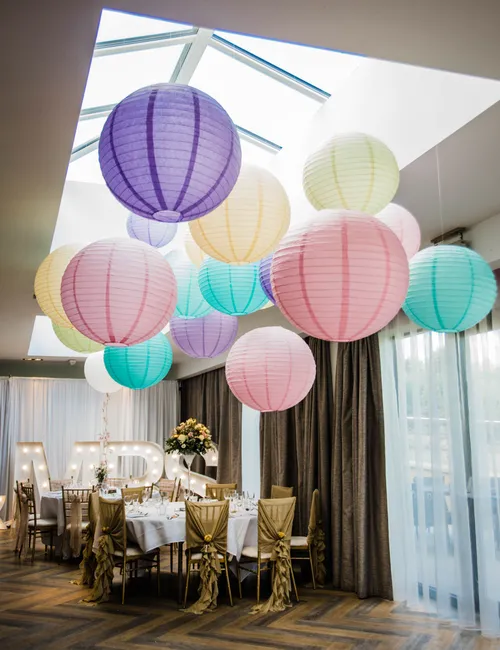 Colourful paper lanterns suspended beneath a skylight above an elegantly decorated wedding reception table.