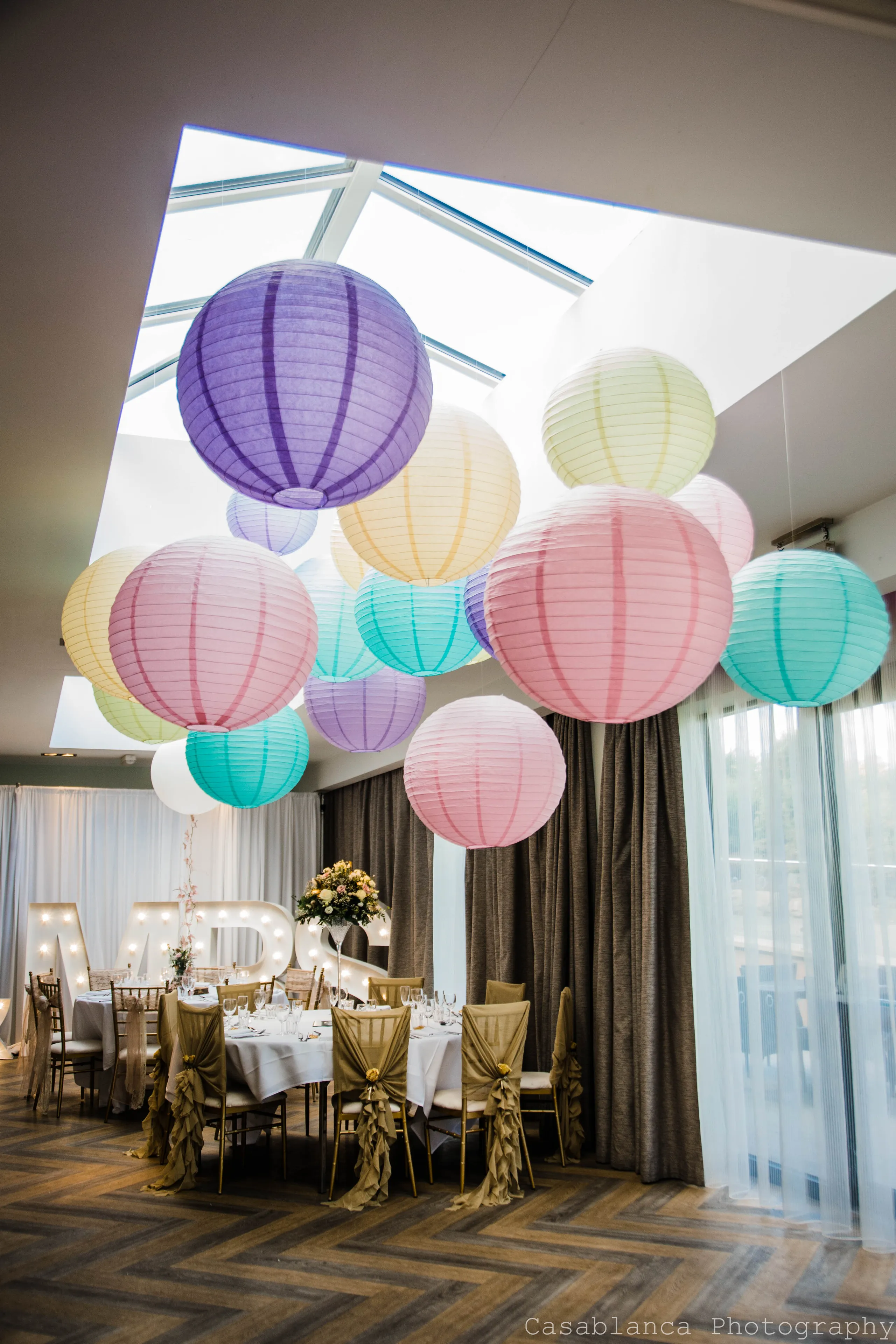 Colourful paper lanterns suspended beneath a skylight above an elegantly decorated wedding reception table.