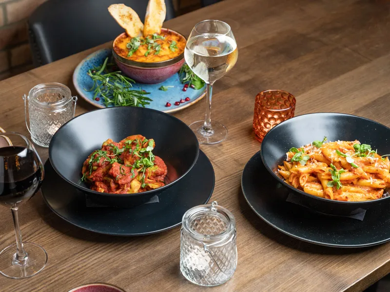 Wooden restaurant table set with colourful pasta dishes, wine glasses and candle holders.