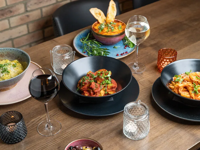 Wooden restaurant table set with colourful pasta dishes, wine glasses and candle holders.