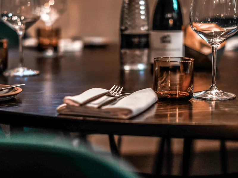 Warmly lit restaurant table set with wine glasses, a bottle, folded napkins and cutlery.