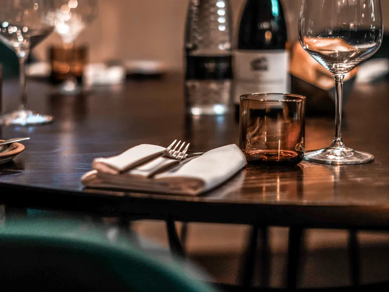 Warmly lit restaurant table set with wine glasses, a bottle, folded napkins and cutlery.