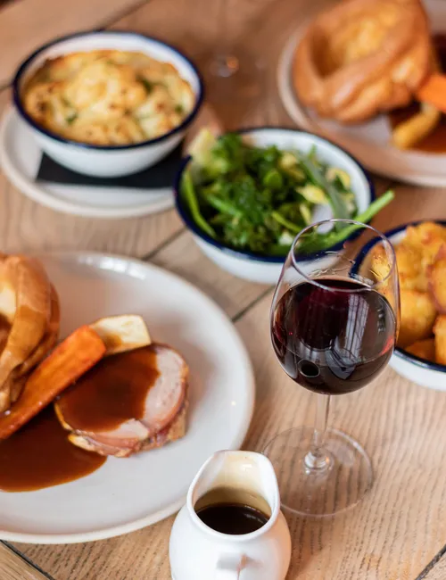 Roast dinner with gravy, vegetables, Yorkshire puddings and a glass of red wine on a wooden table