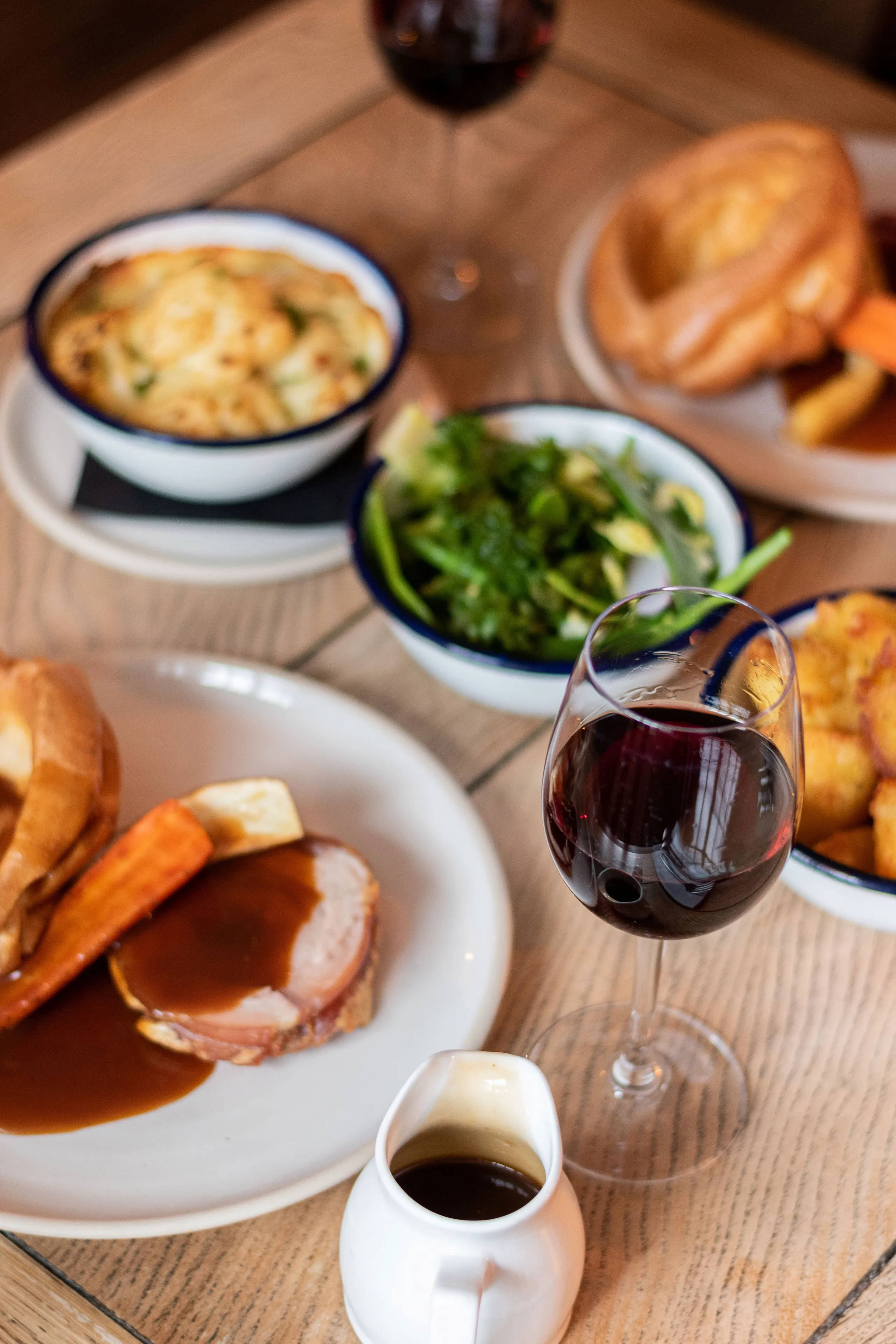 Roast dinner with gravy, vegetables, Yorkshire puddings and a glass of red wine on a wooden table