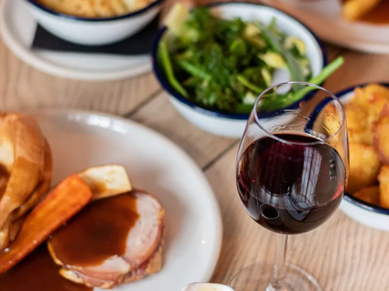Roast dinner with gravy, vegetables, Yorkshire puddings and a glass of red wine on a wooden table