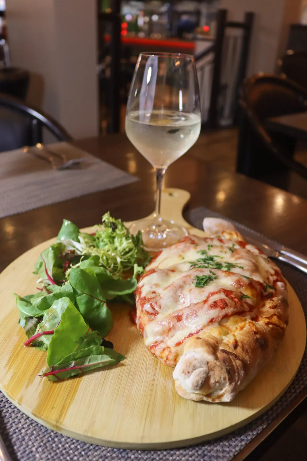 Cheese-topped stuffed bread roll served with mixed salad and a glass of white wine in a restaurant.
