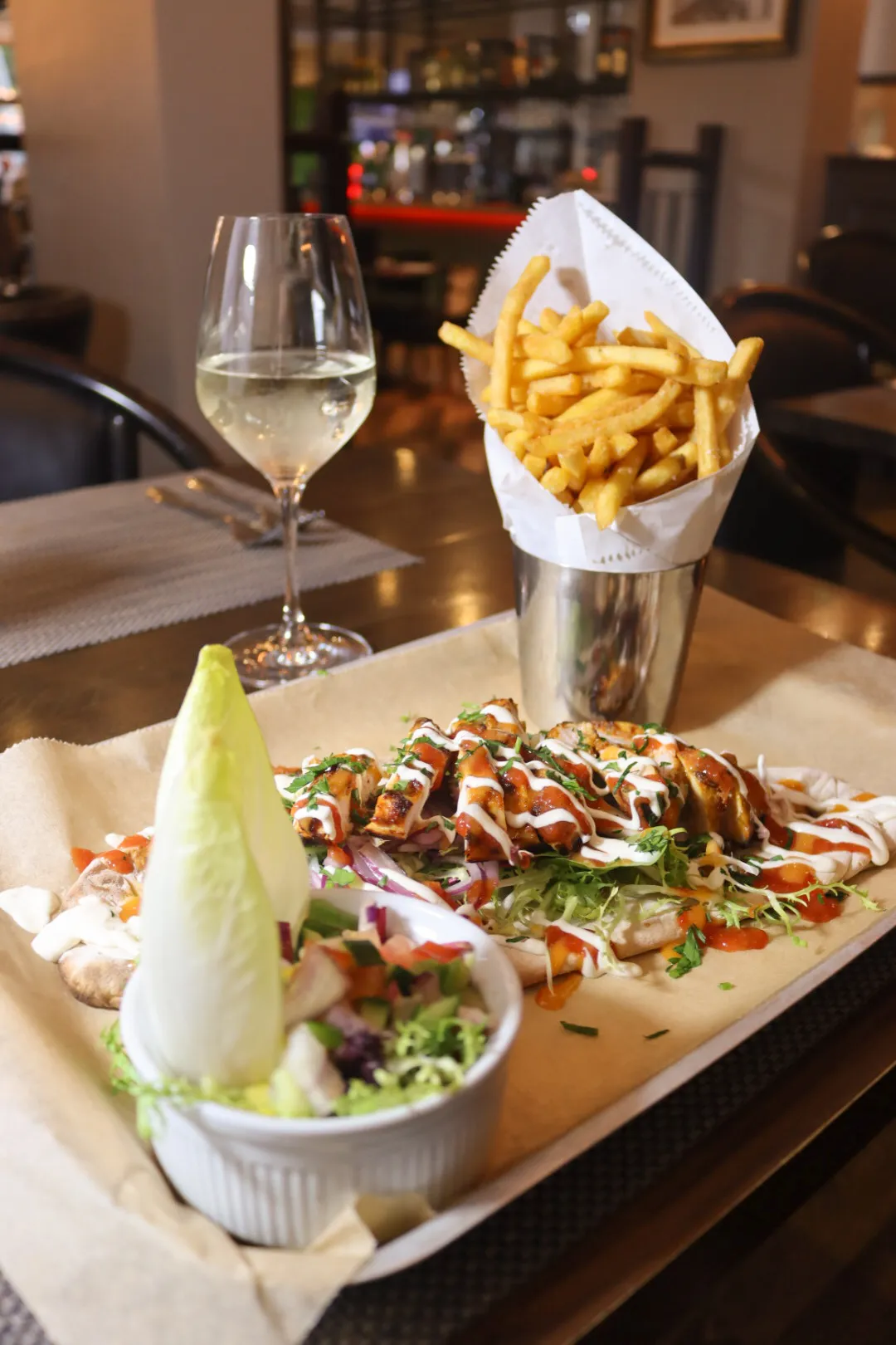 Grilled chicken flatbread with salad, chips and a glass of white wine in a restaurant