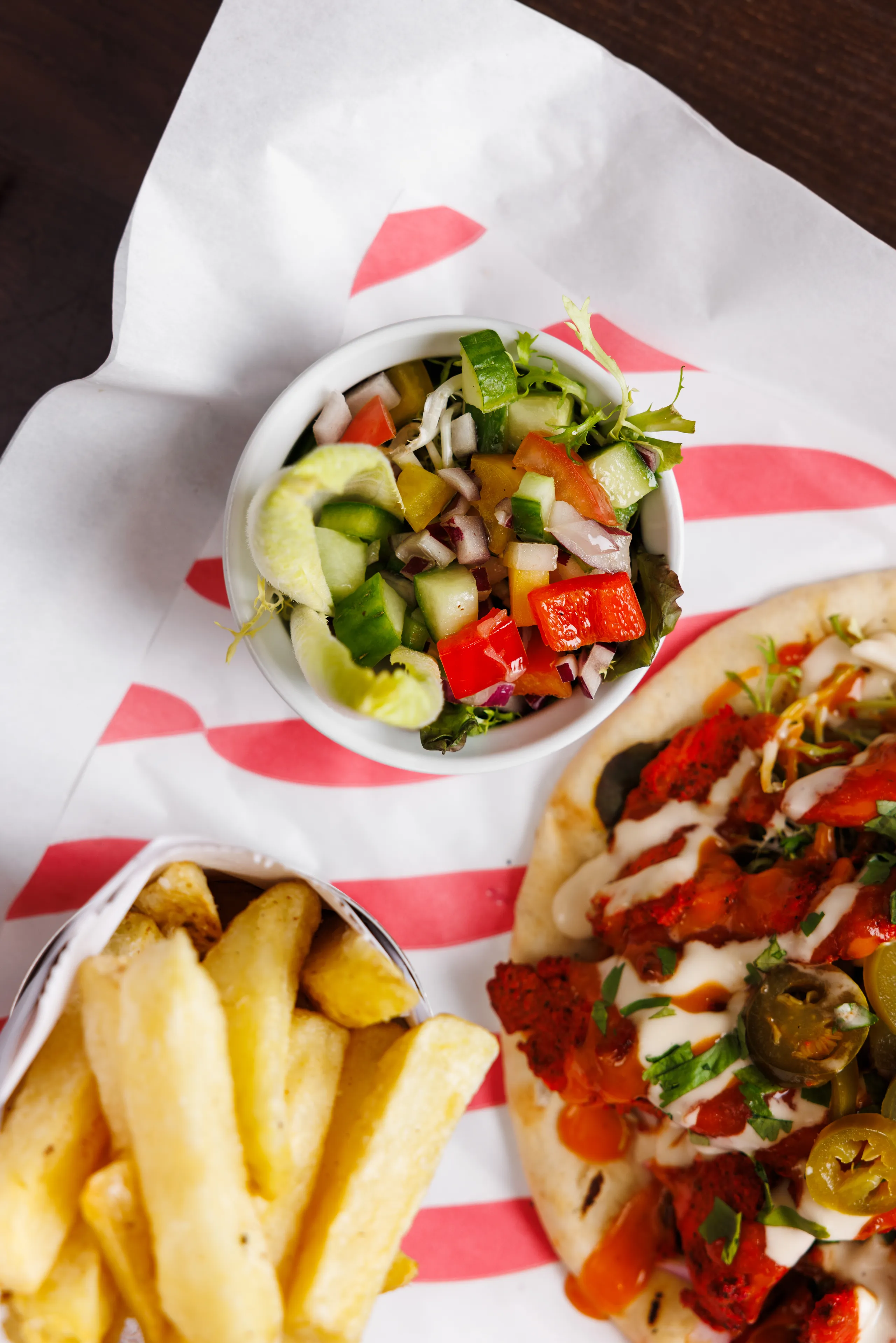 Loaded flatbread with spicy toppings, chips and a fresh mixed salad in a takeaway tray