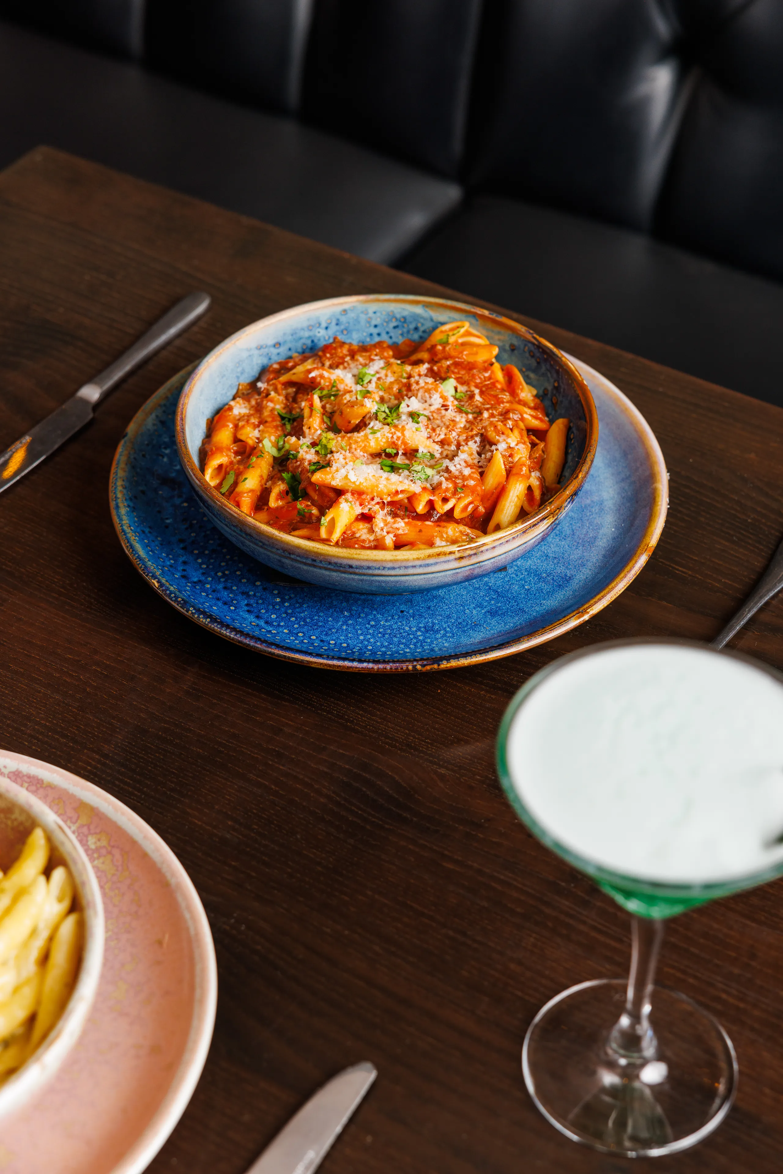 Penne pasta in rich tomato sauce topped with grated cheese and herbs in a blue ceramic bowl