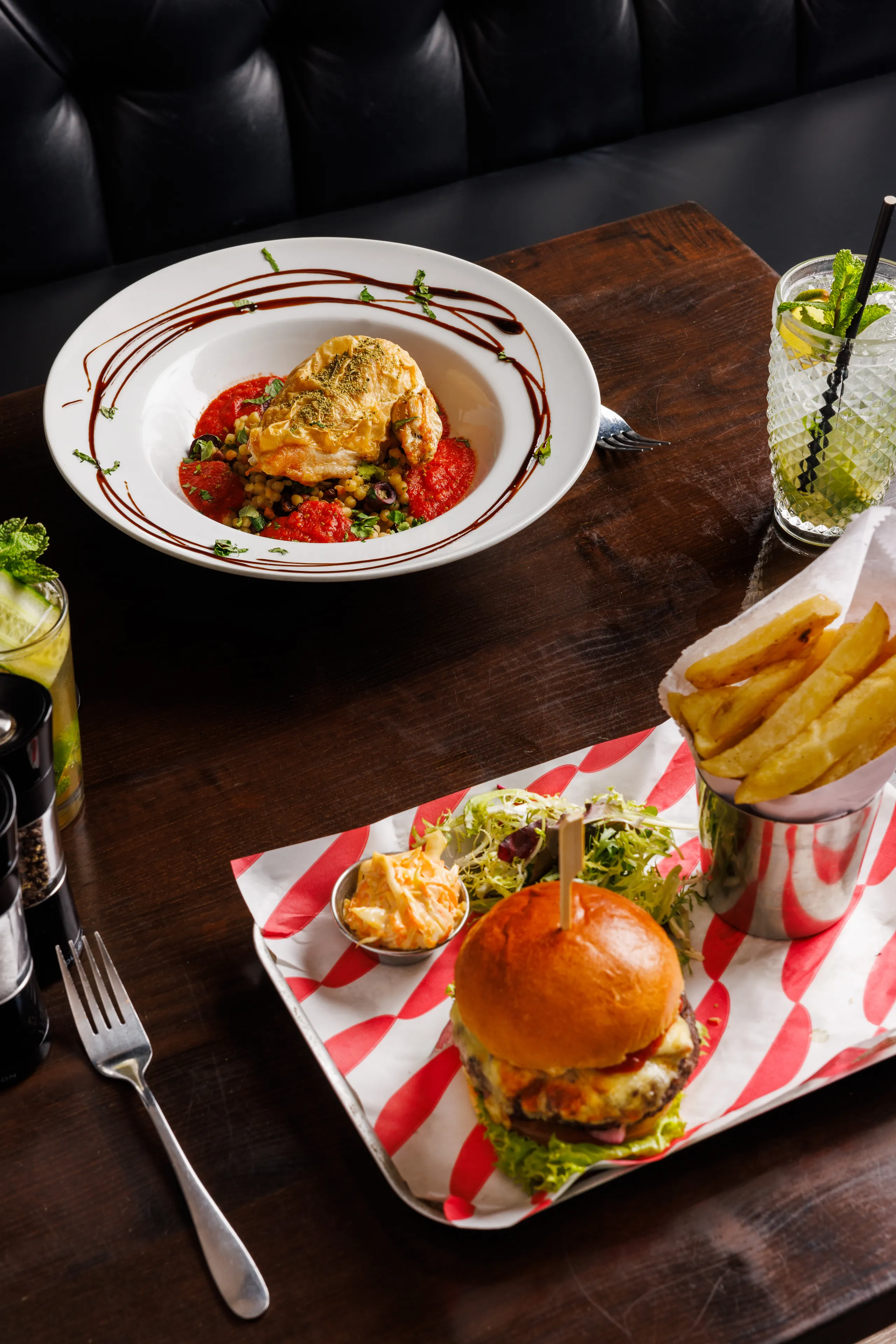 Gourmet burger with chips, salad and a plated chicken dish on a wooden restaurant table
