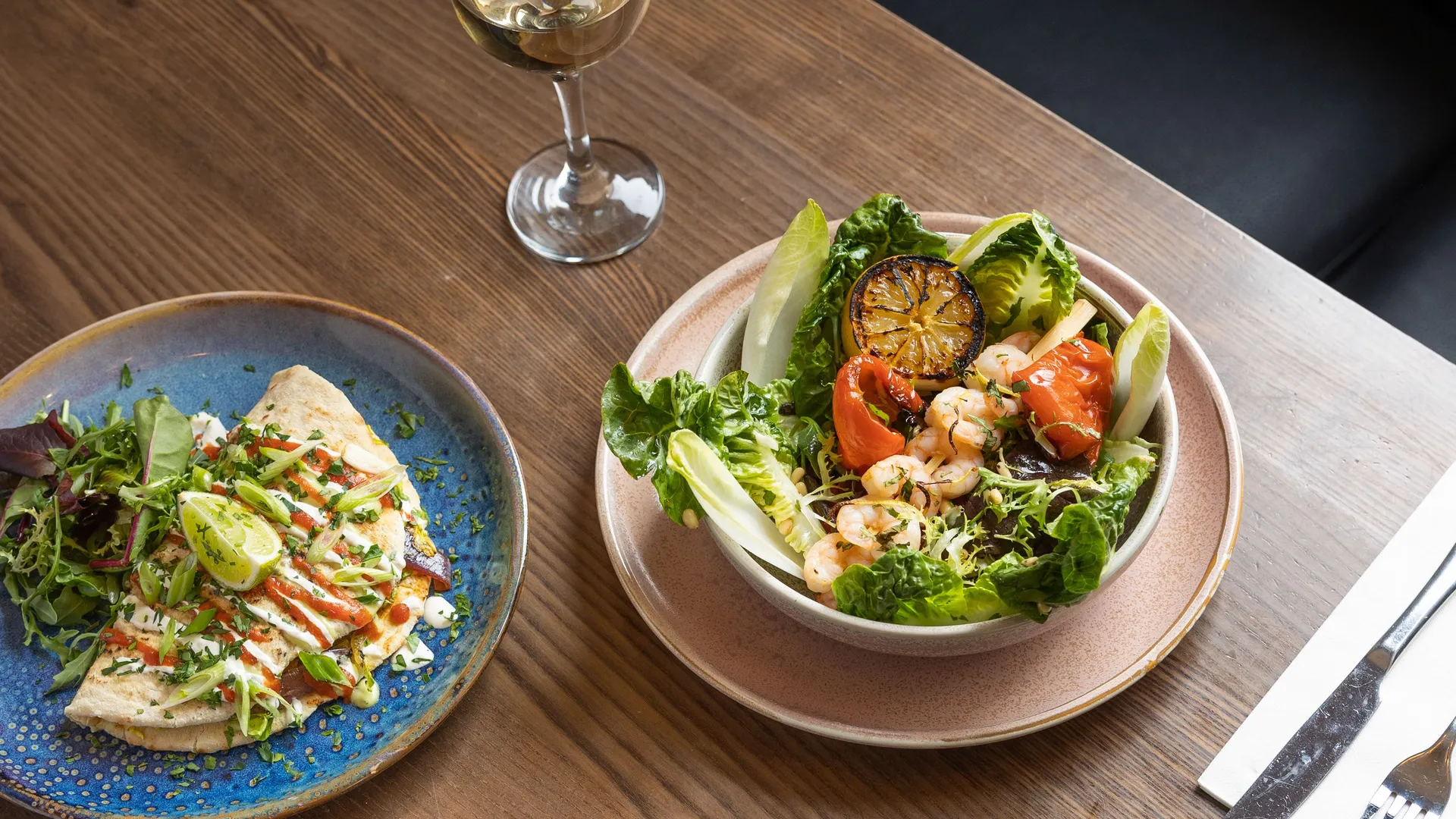Assorted fresh salads and seafood dishes served on a wooden restaurant table with a glass of white wine