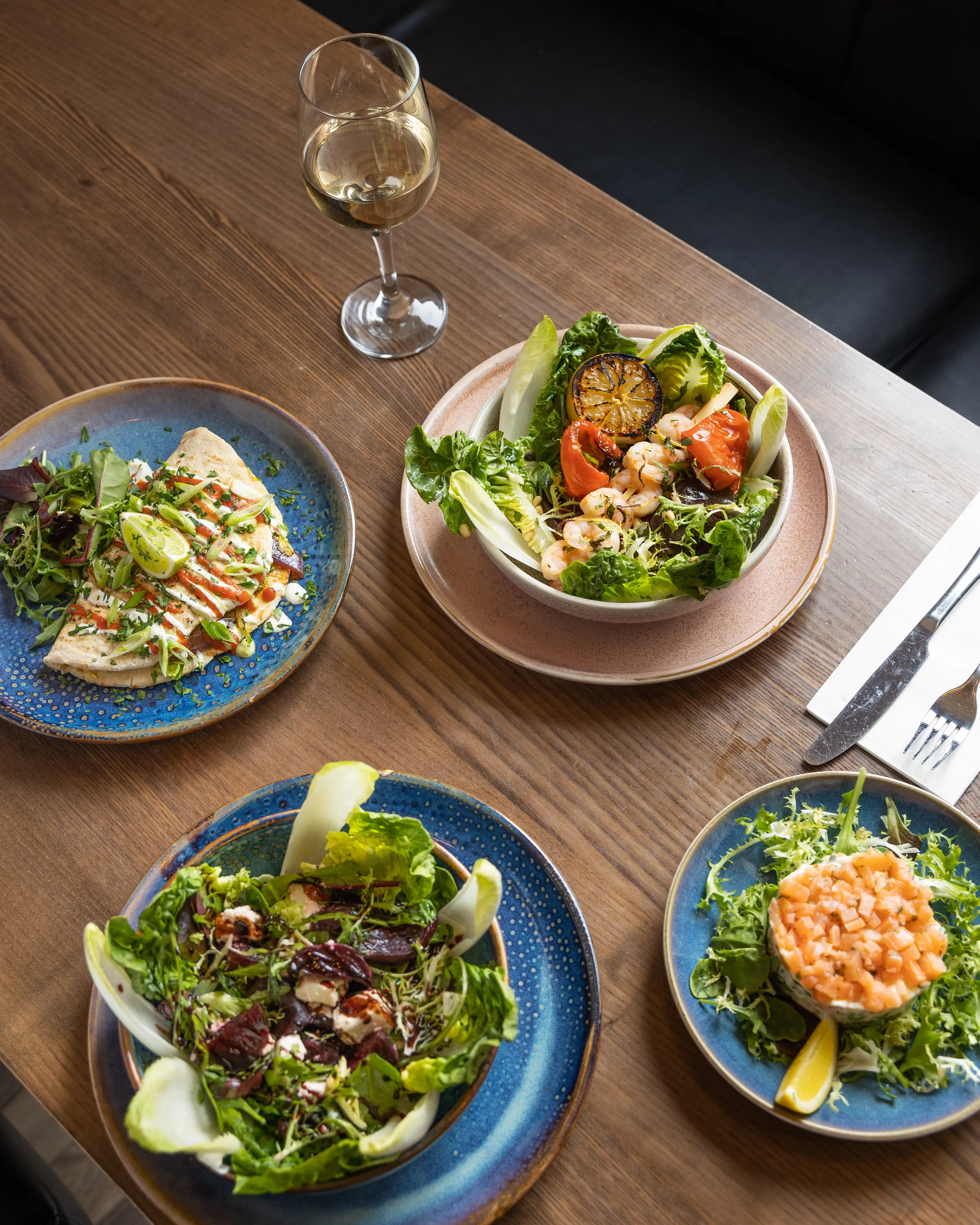 Assorted fresh salads and seafood dishes served on a wooden restaurant table with a glass of white wine