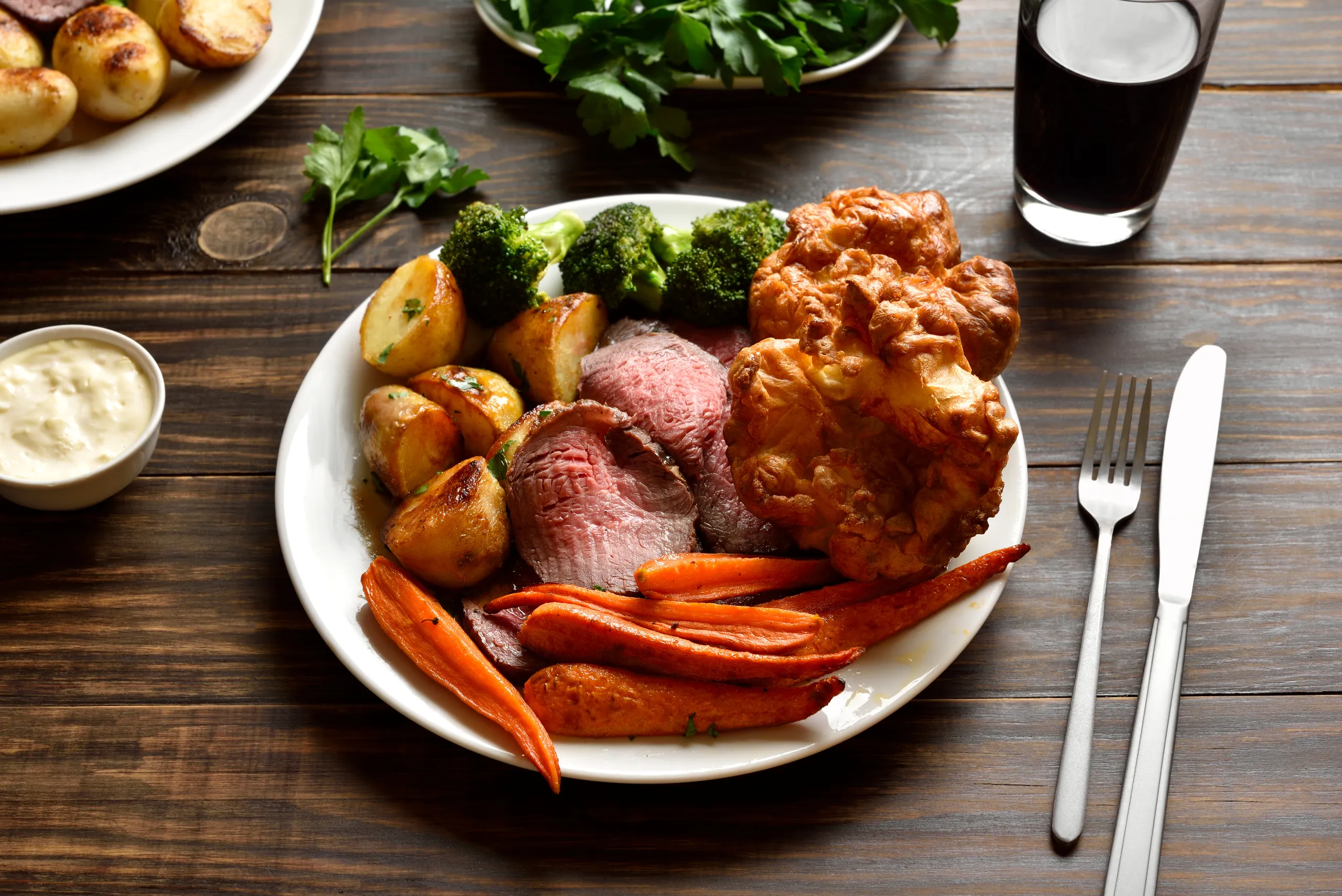 Roast beef dinner with Yorkshire pudding, roasted potatoes, carrots and broccoli on a white plate.