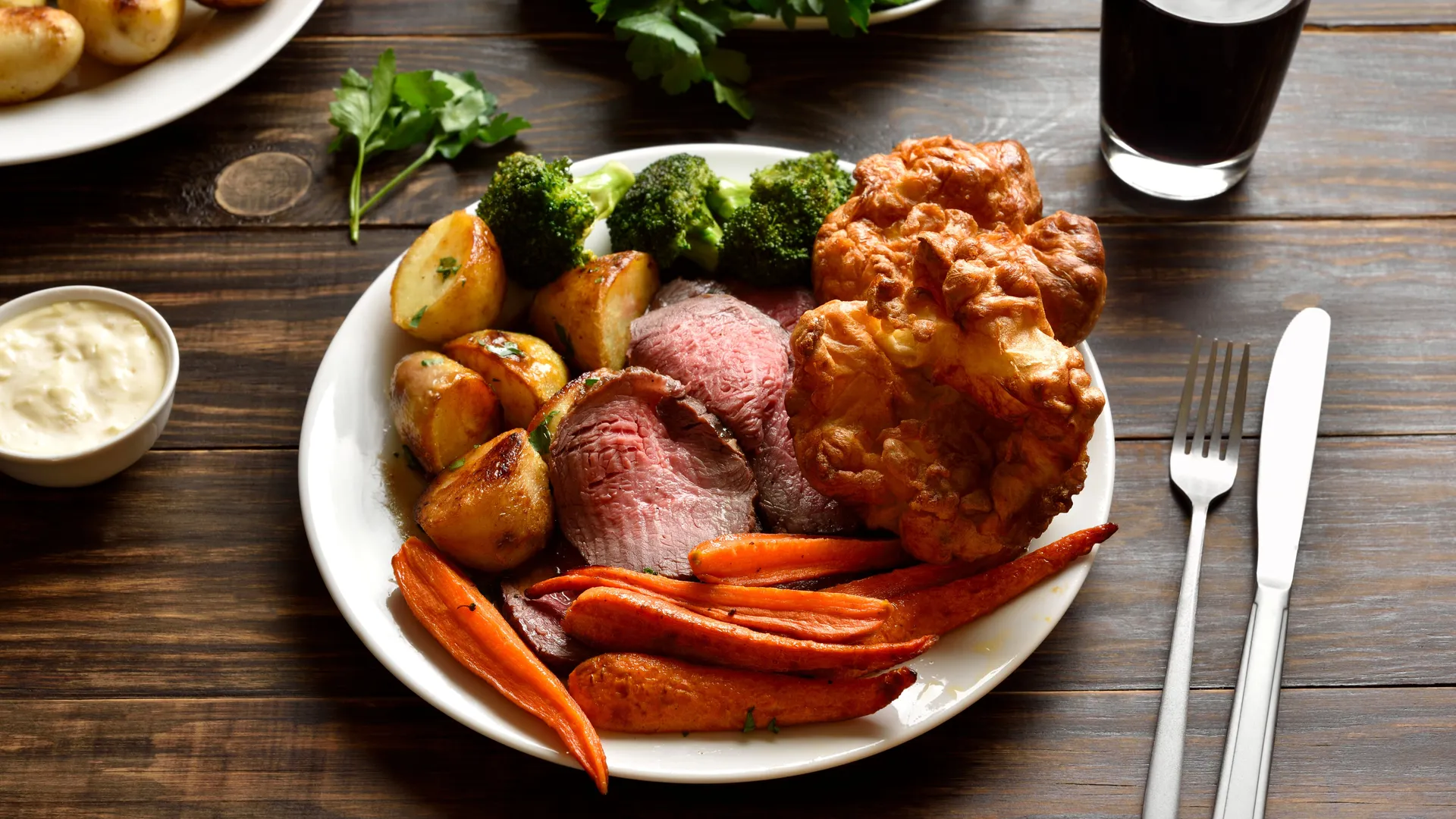 Roast beef dinner with Yorkshire pudding, roasted potatoes, carrots and broccoli on a white plate.