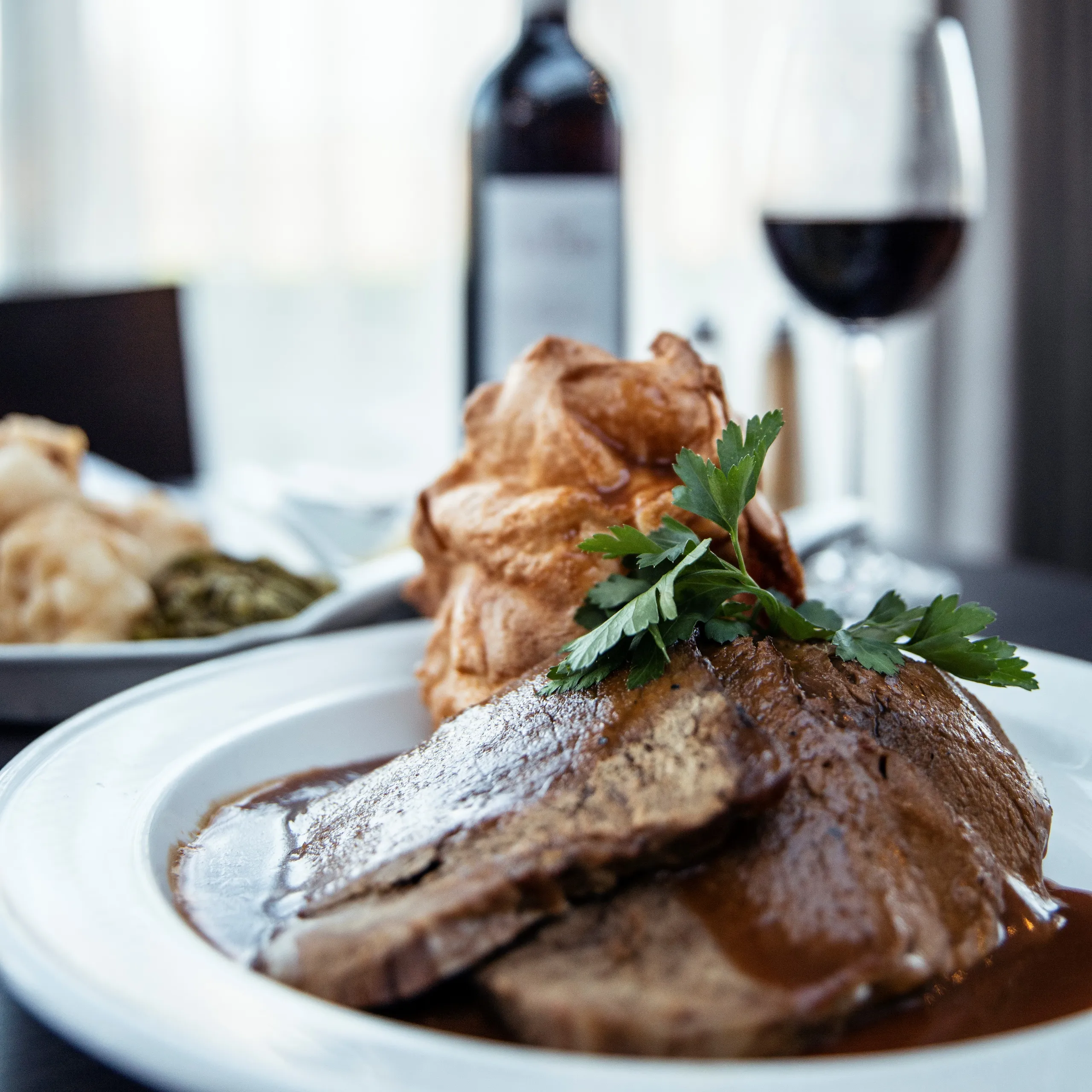 Sliced roast beef with gravy and parsley, served with Yorkshire pudding and red wine.