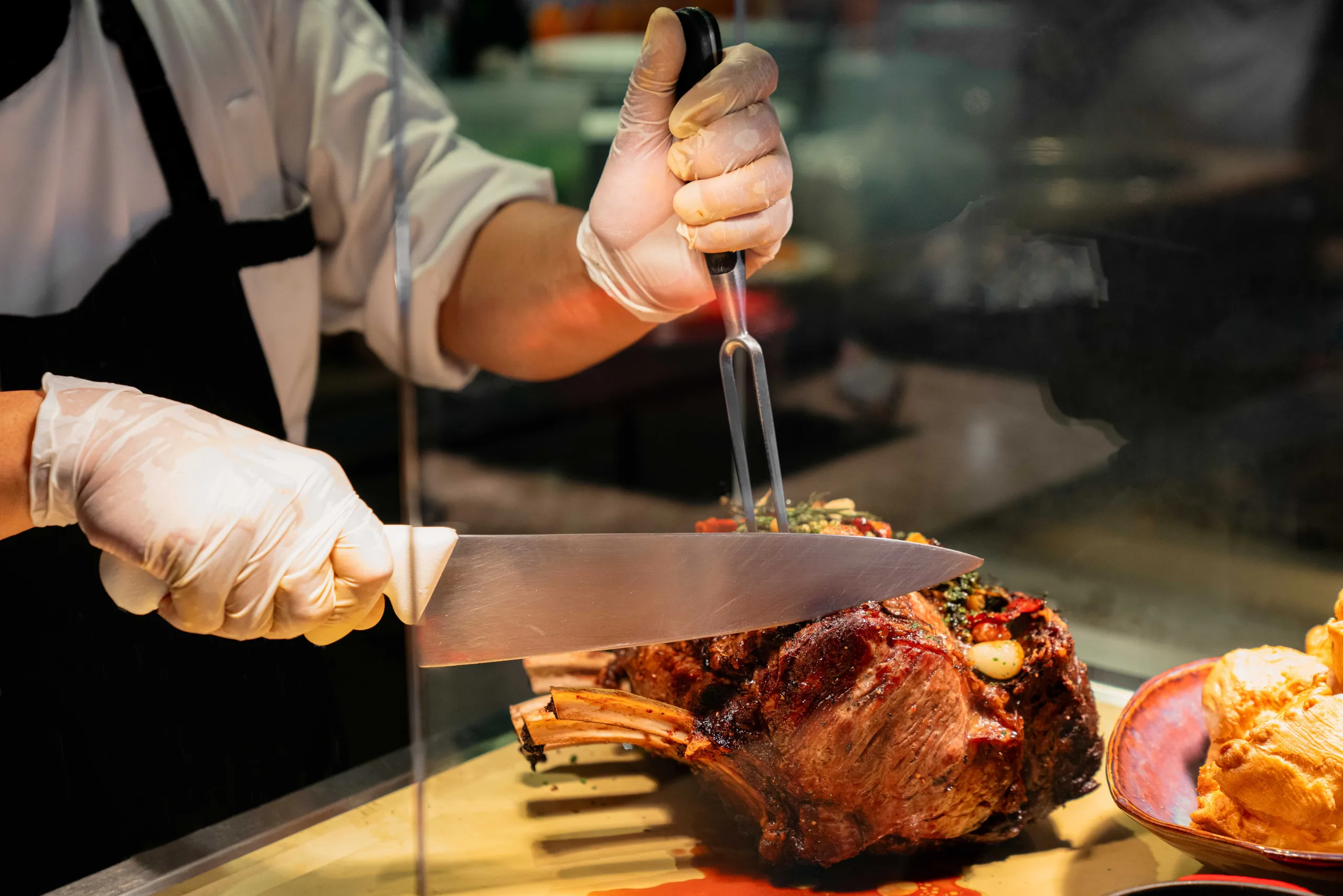 Chef carving a roasted bone-in joint of meat behind a buffet counter