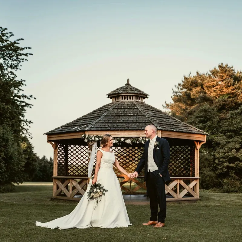 Bride and groom holding hands in front of a flower-decorated wooden gazebo at an outdoor wedding.