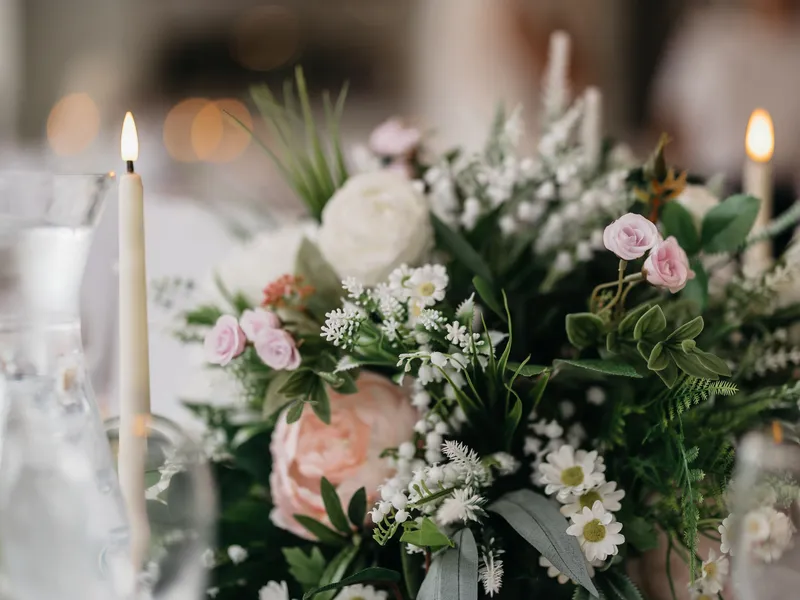 Romantic floral table centrepiece with pink and white flowers, greenery and lit taper candles.