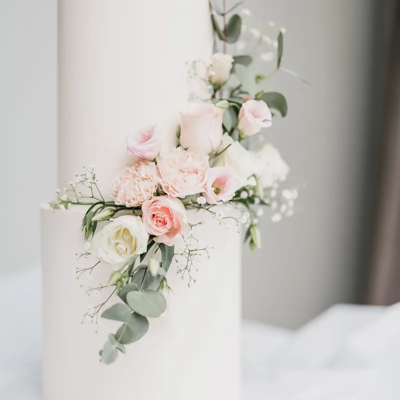 Elegant white two-tier wedding cake decorated with cascading blush roses, carnations, baby's breath and eucalyptus foliage.