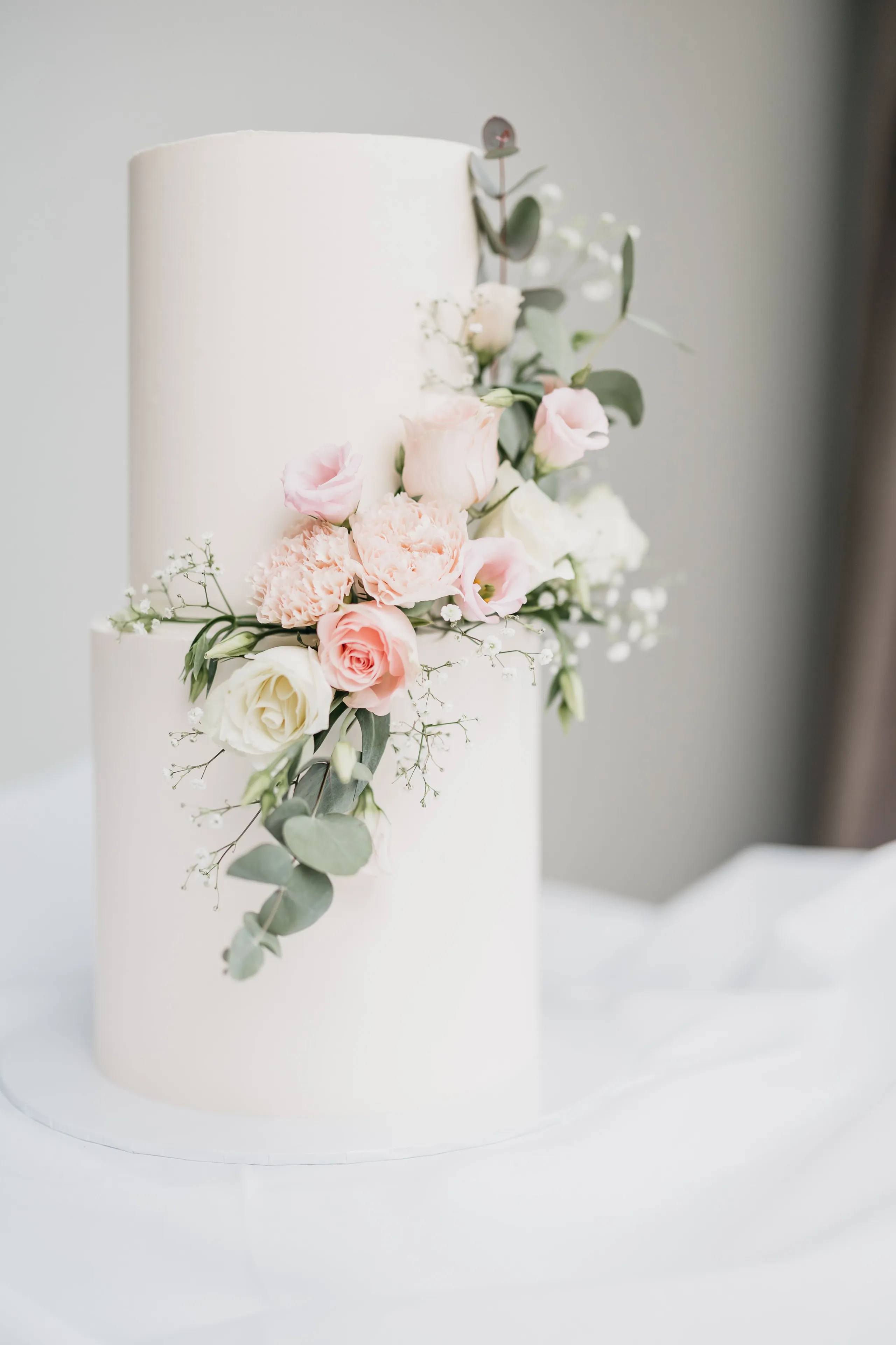 Elegant white two-tier wedding cake decorated with cascading blush roses, carnations, baby's breath and eucalyptus foliage.