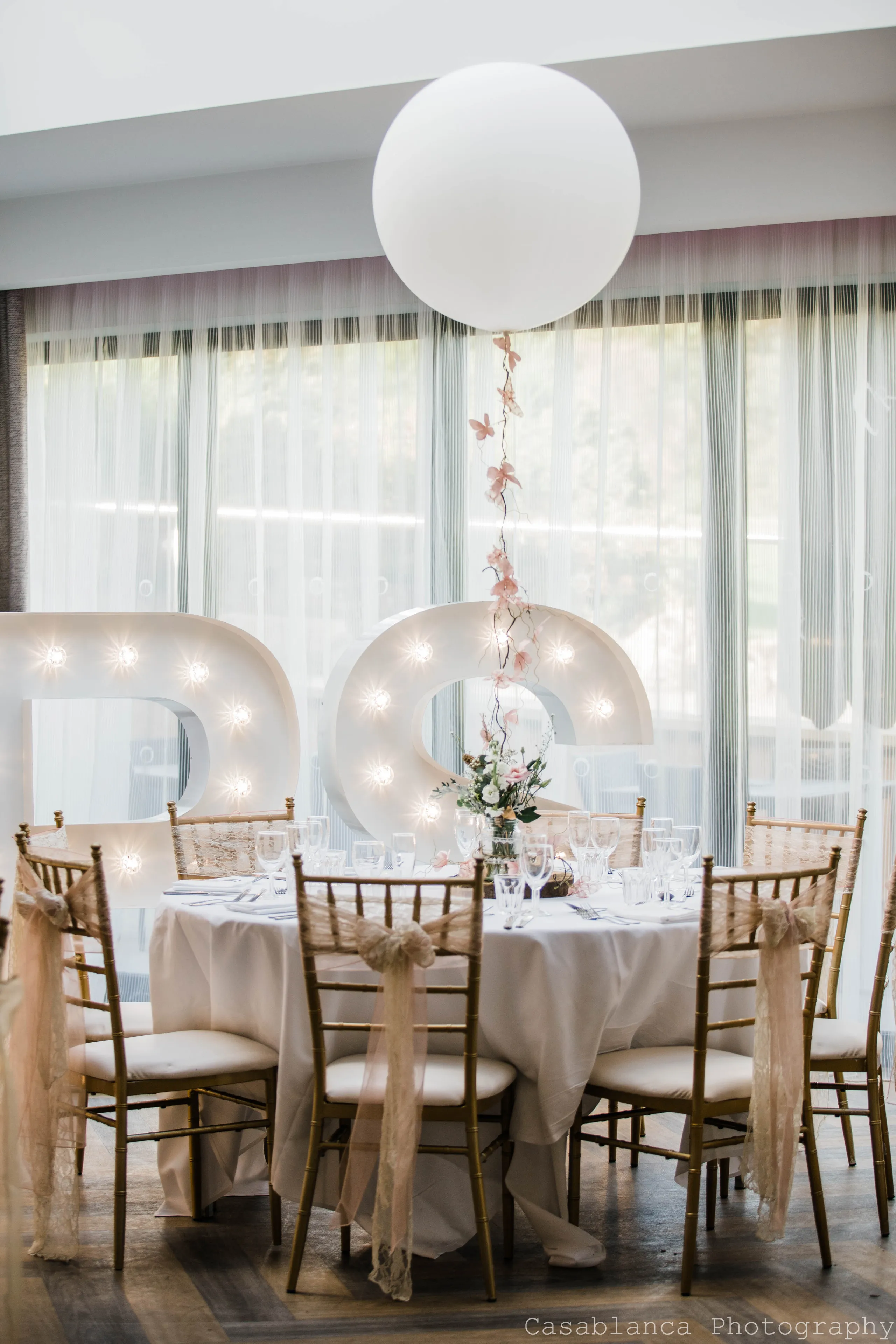 Large white balloon centrepiece above an elegantly dressed wedding table with illuminated love letters
