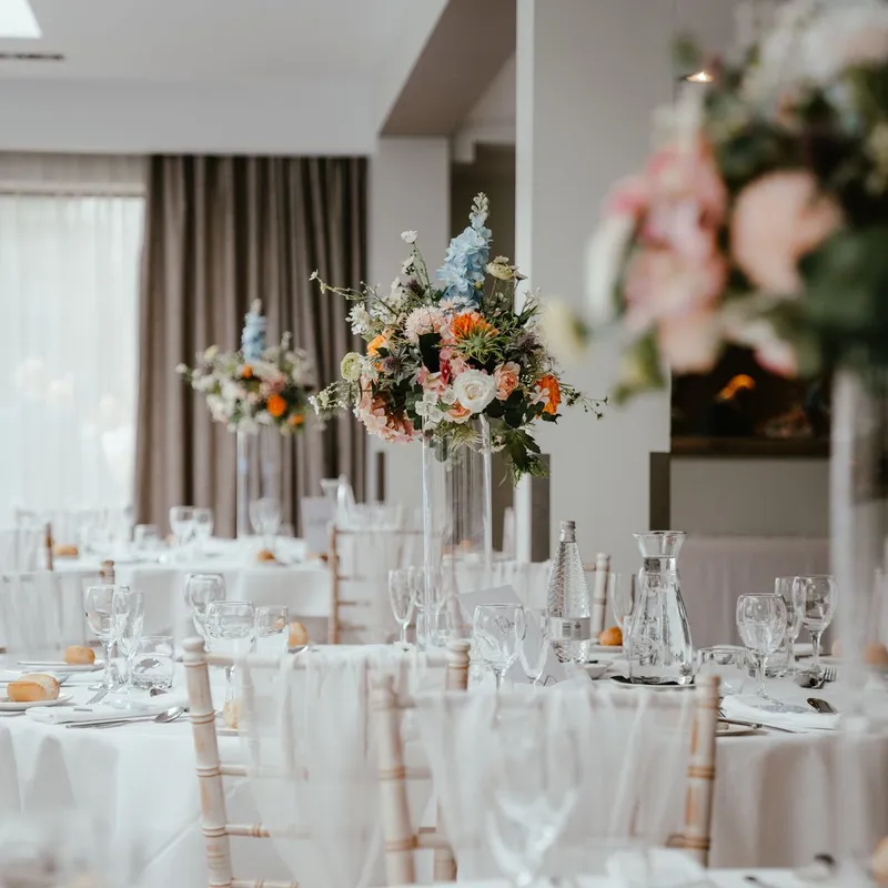 Elegant wedding reception tables with tall colourful floral centrepieces in a bright orangery