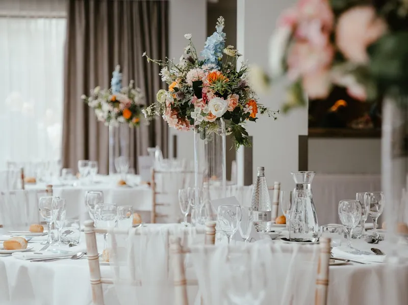 Elegant wedding reception tables with tall colourful floral centrepieces in a bright orangery