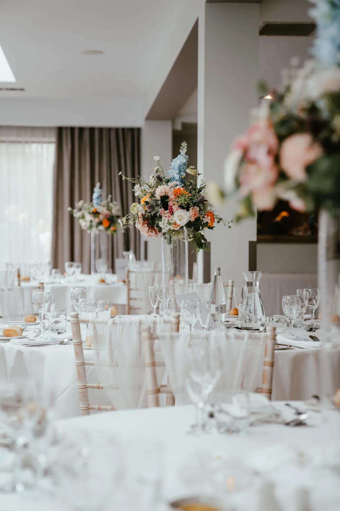Elegant wedding reception tables with tall colourful floral centrepieces in a bright orangery