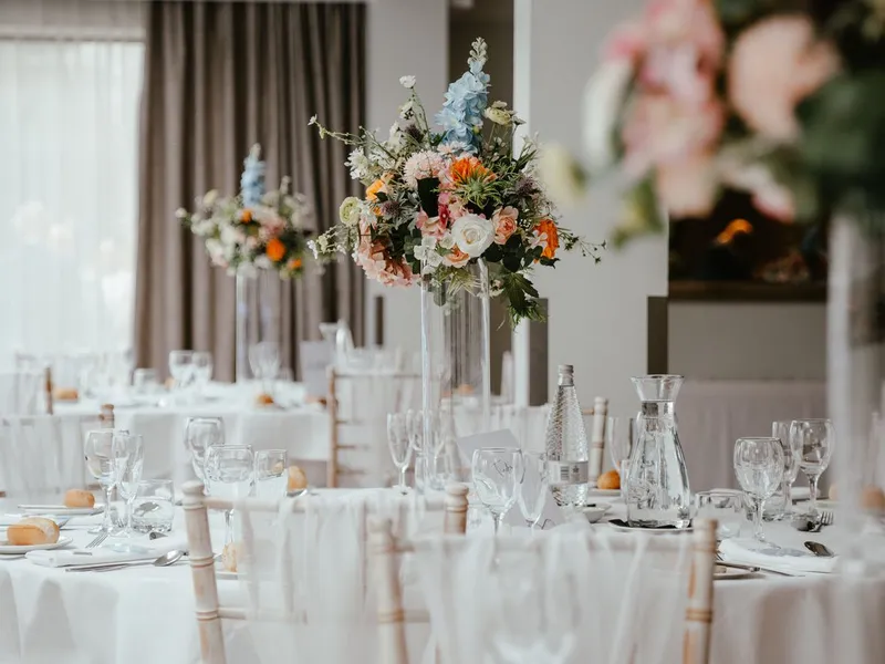 Elegant wedding reception tables with tall colourful floral centrepieces in a bright orangery