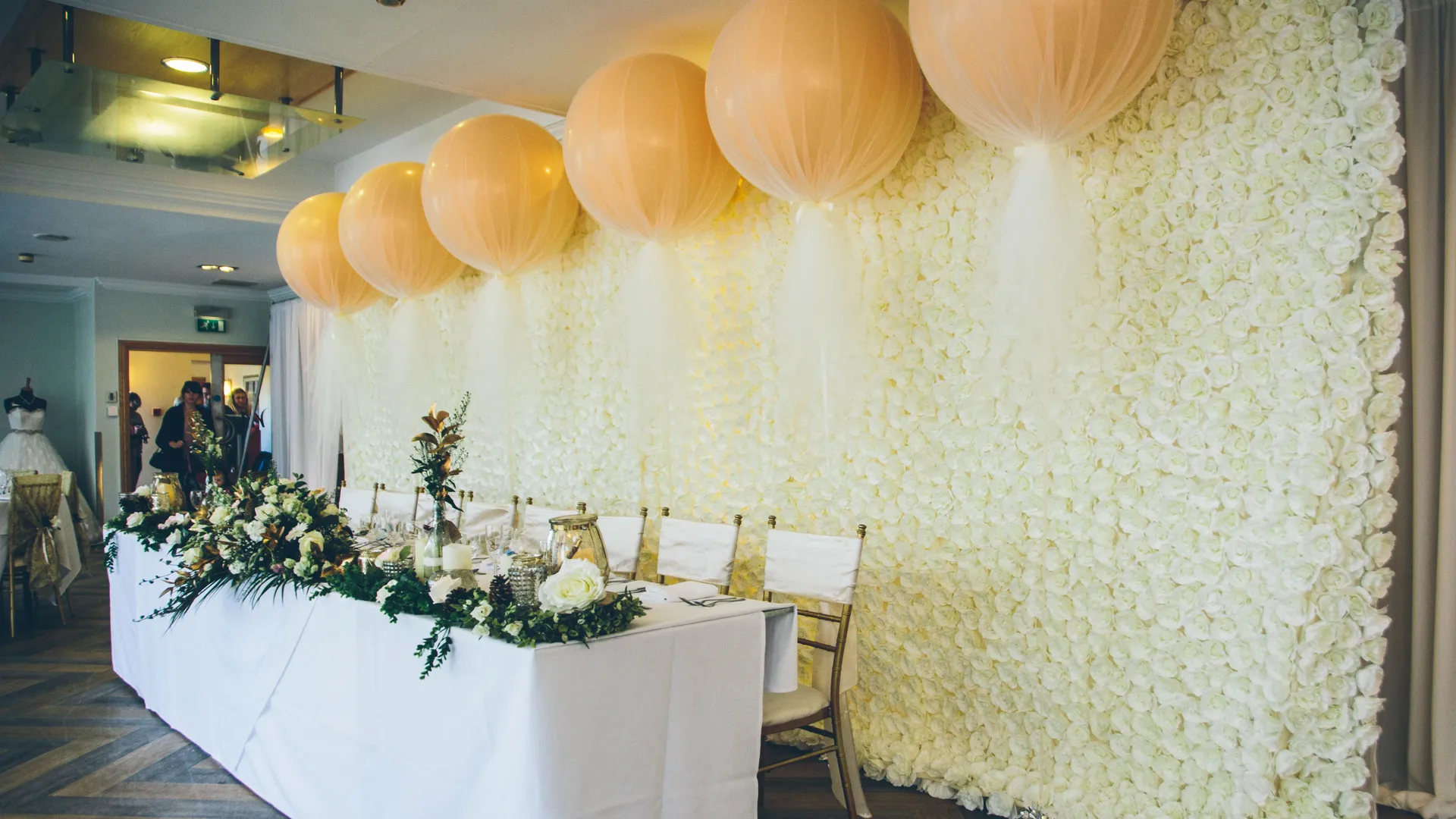 Elegant wedding top table with white floral wall, greenery arrangements and peach hanging lanterns.