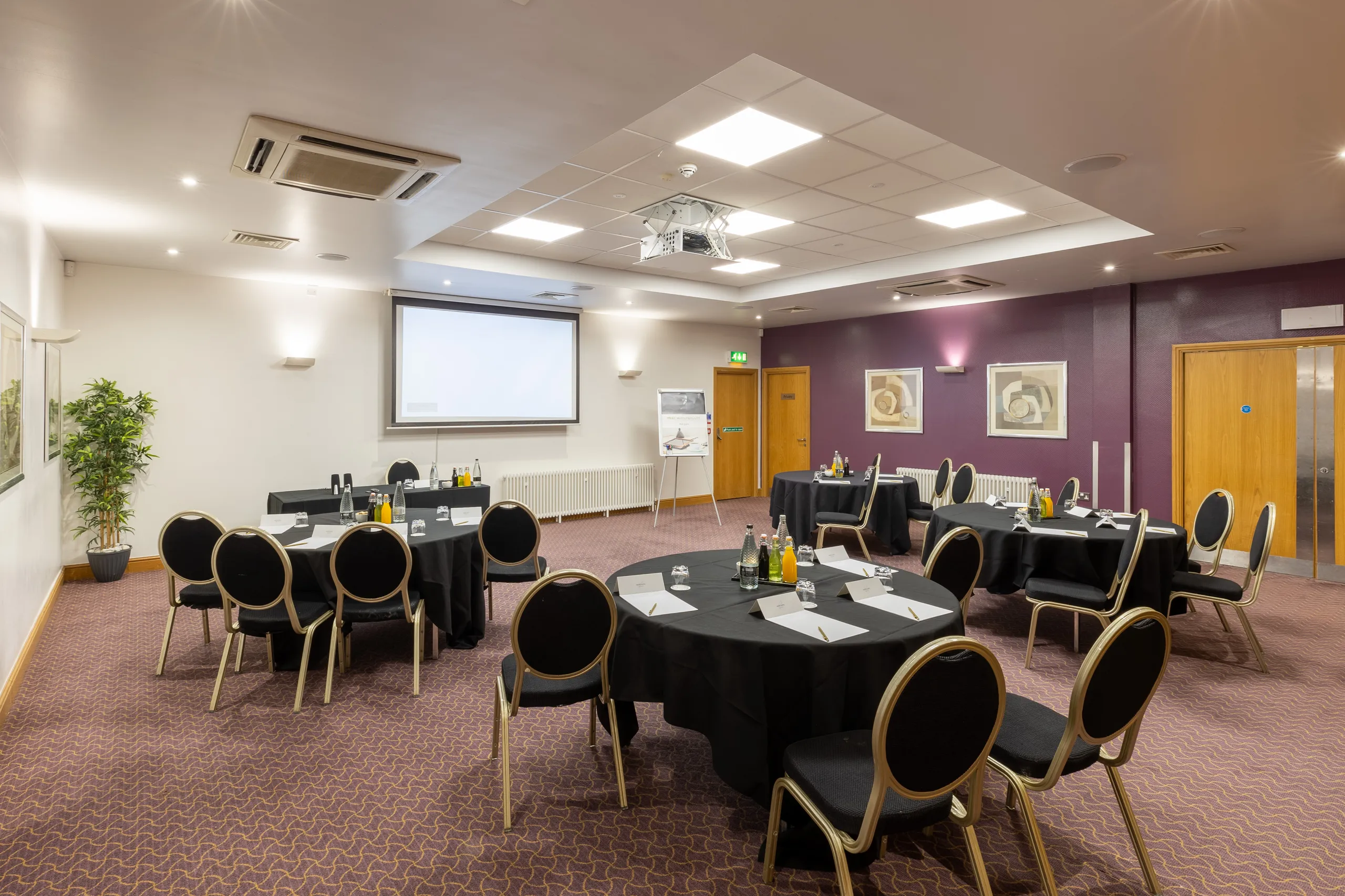 Modern conference room with round tables, black chairs, projector screen and presentation equipment