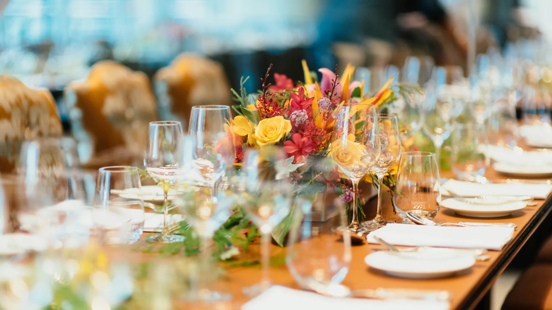 Elegantly laid dining table with wine glasses, white plates and a colourful floral centrepiece.