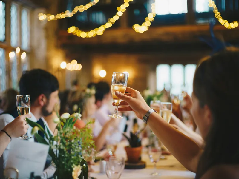 Guests raise champagne glasses in a toast at a warmly lit celebration dinner.