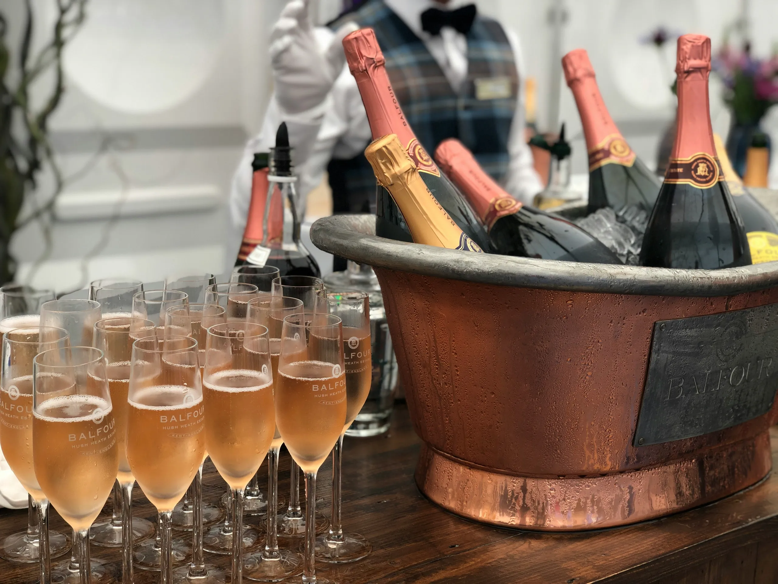 Champagne flutes filled with rosé sparkling wine beside bottles chilling in a copper ice bucket.