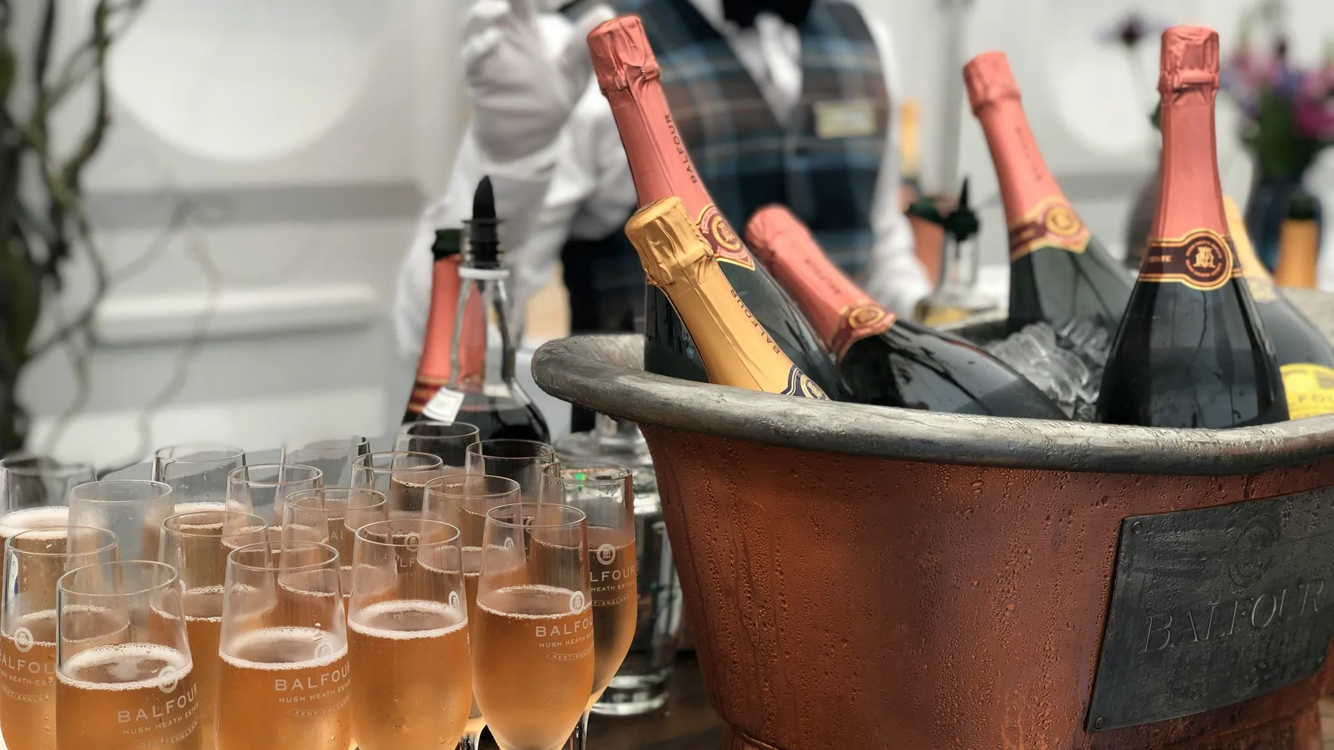 Champagne flutes filled with rosé sparkling wine beside bottles chilling in a copper ice bucket.