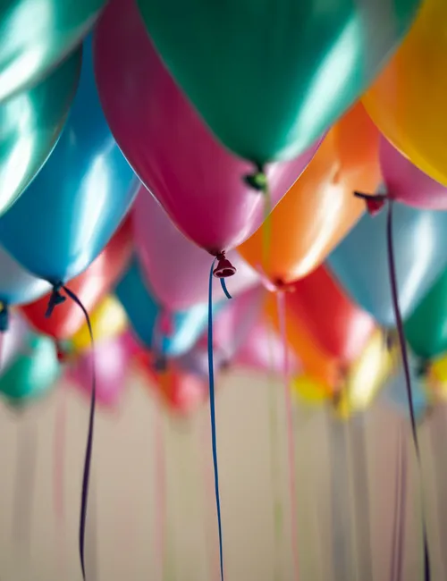 Colourful helium balloons with dangling ribbons filling a party space