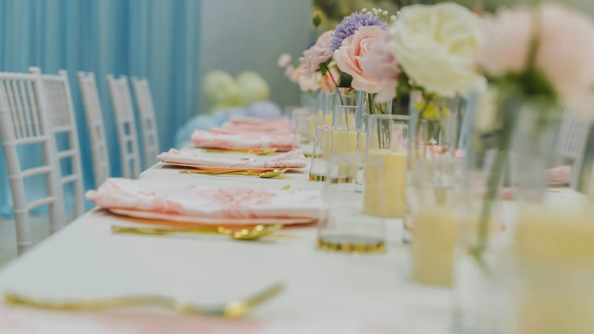 Elegant banquet table set with pastel flowers, gold cutlery and white chairs