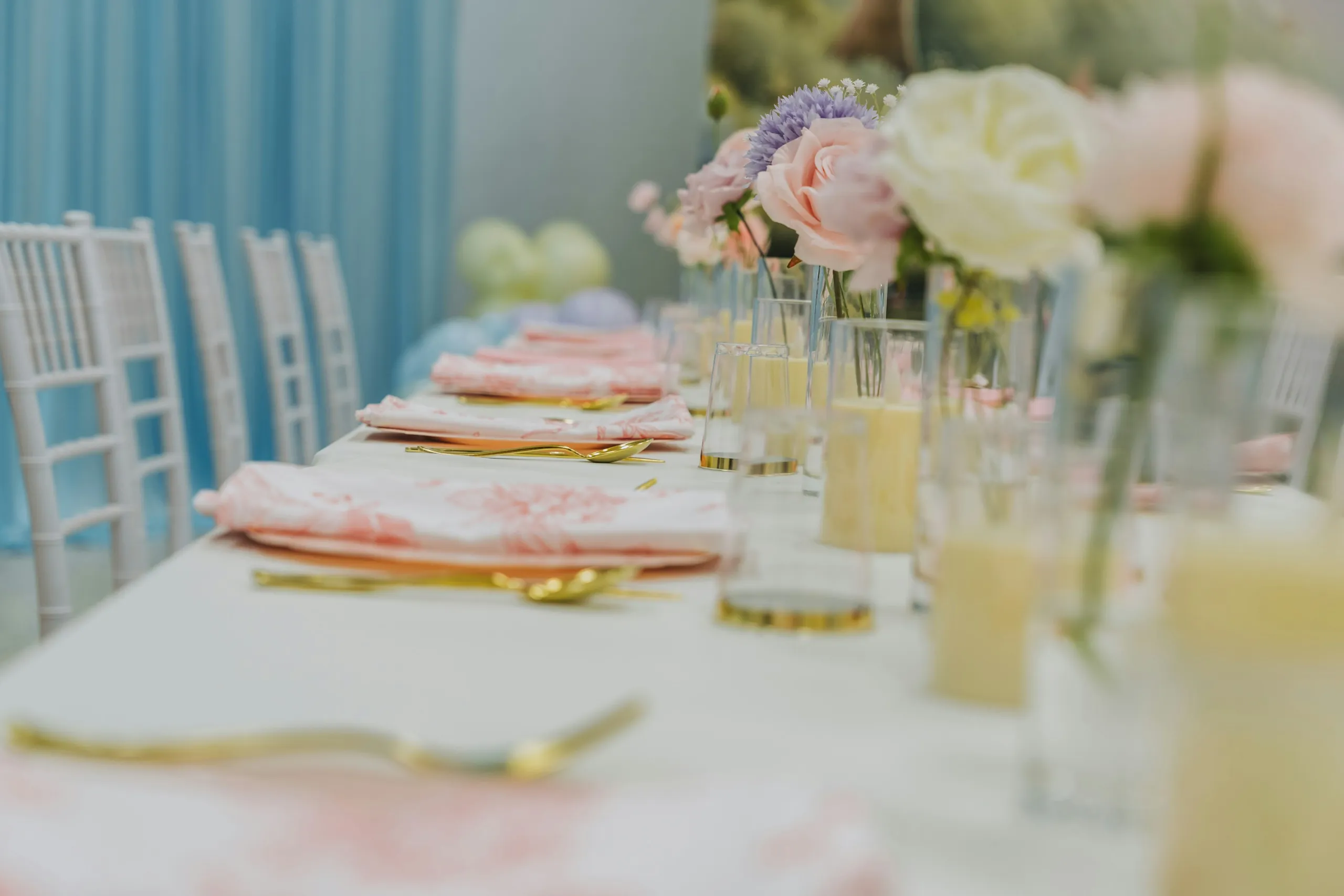 Elegant banquet table set with pastel flowers, gold cutlery and white chairs