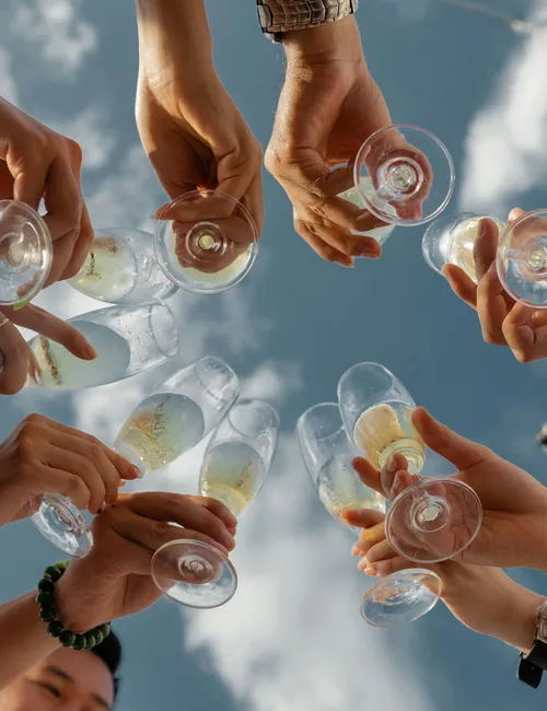 Friends raising champagne glasses in a toast against a bright blue sky on a boat