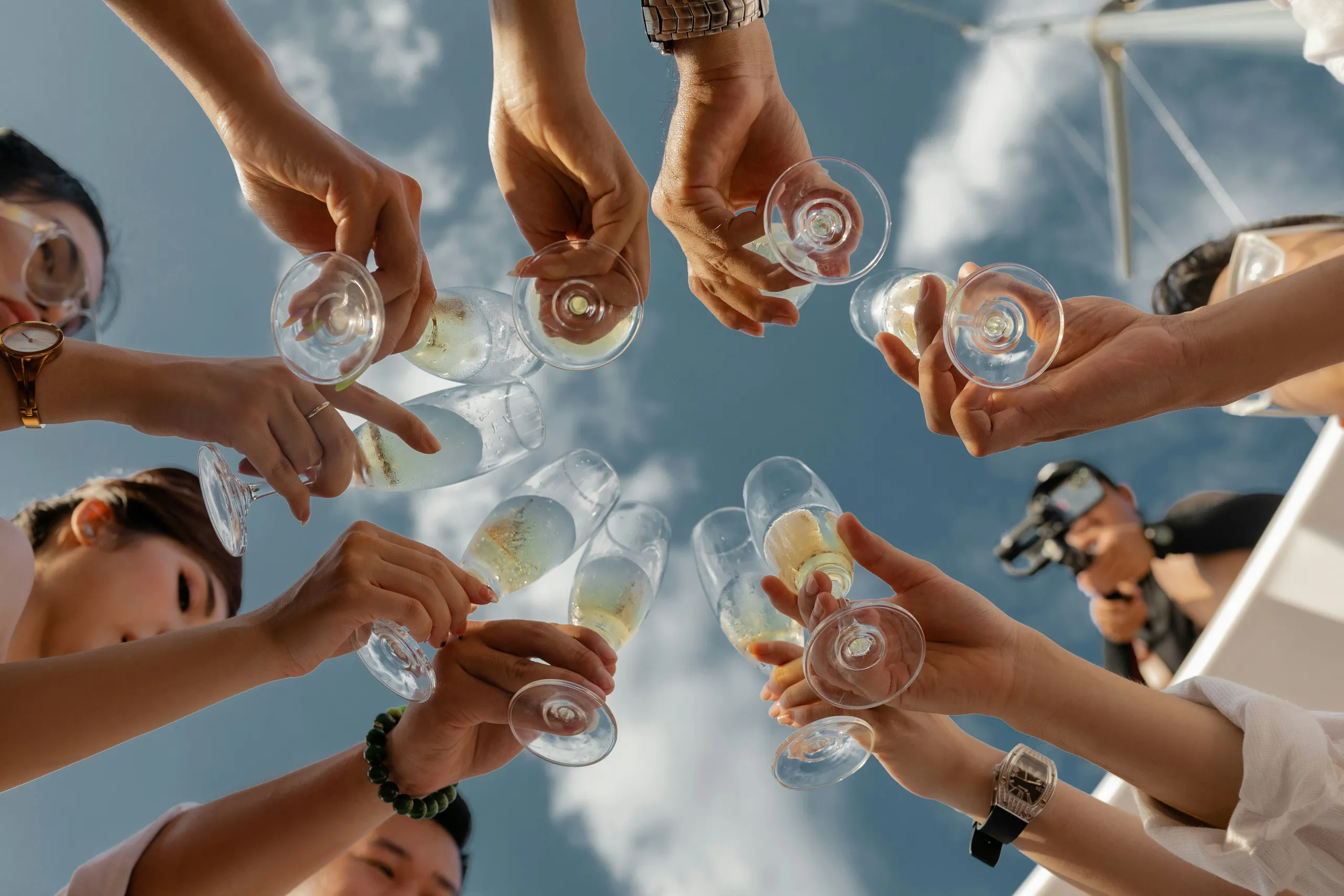 Friends raising champagne glasses in a toast against a bright blue sky on a boat
