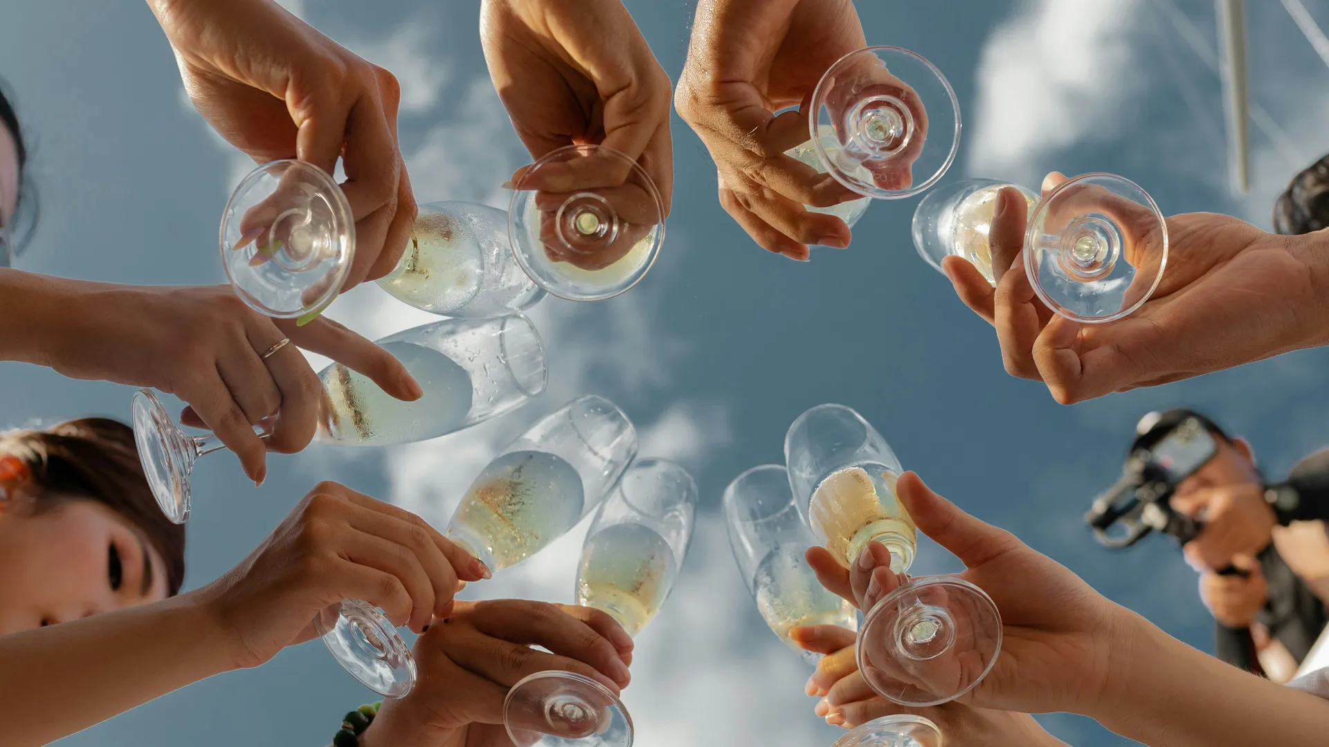 Friends raising champagne glasses in a toast against a bright blue sky on a boat