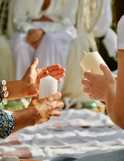 Two people holding white candles during an outdoor gathering, with one candle lit.