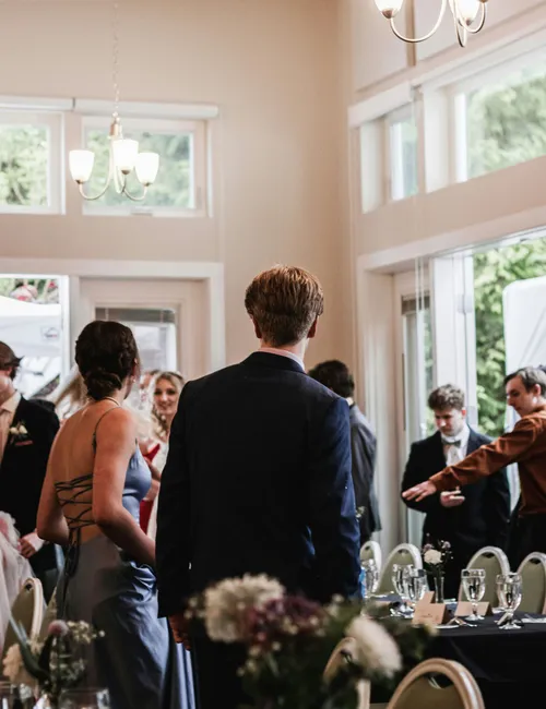 Wedding guests gathered in an elegant reception hall with chandeliers and dressed tables.
