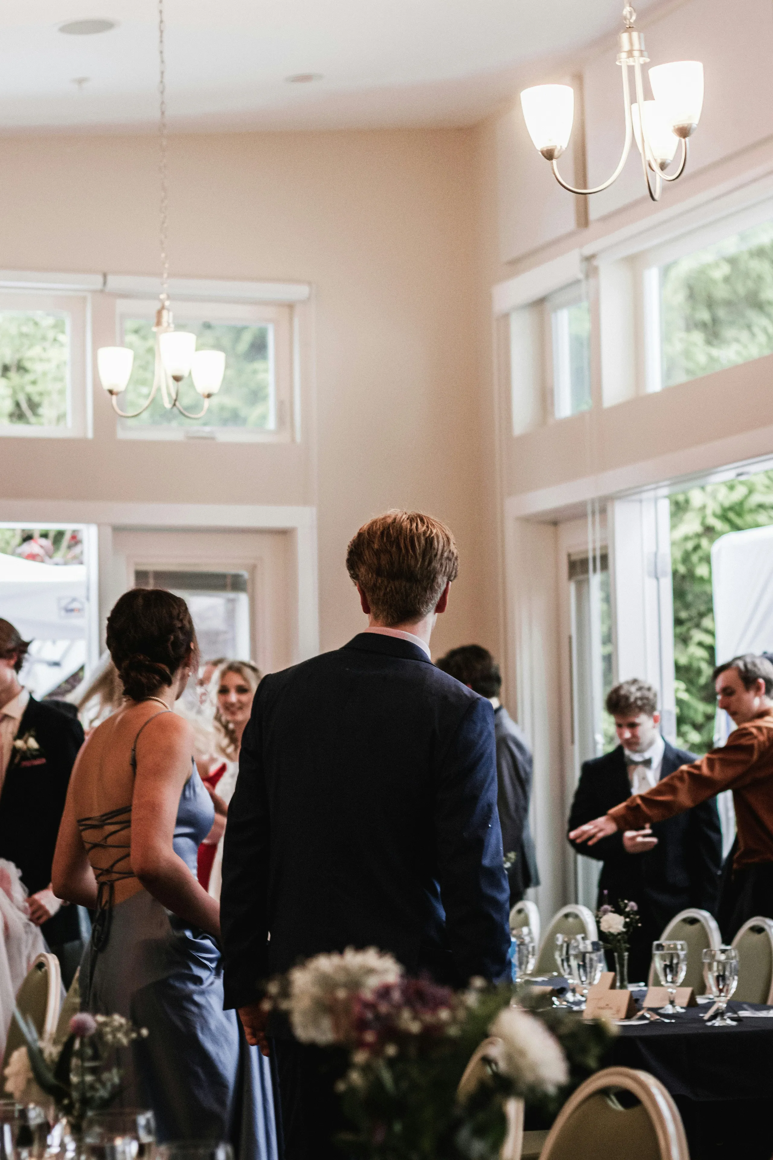 Wedding guests gathered in an elegant reception hall with chandeliers and dressed tables.